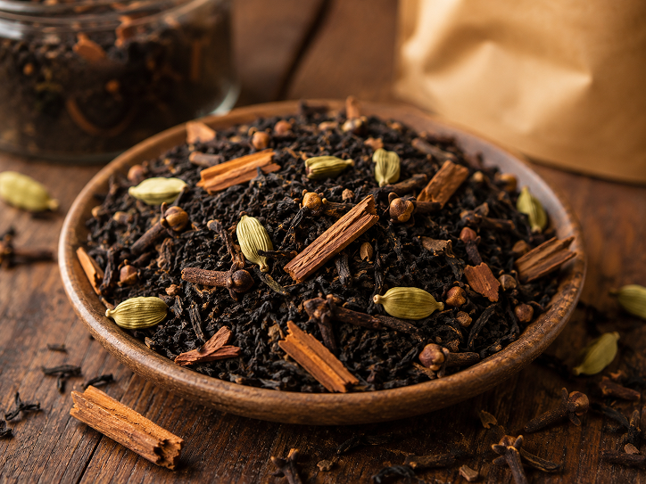 Loose leaf chai tea with whole spices including cardamom cinnamon and cloves in a wooden bowl