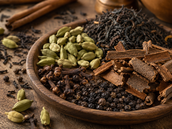 Whole chai spices including cardamom pods green cinnamon sticks cloves and black pepper on a dark background